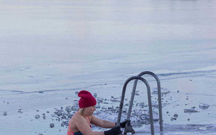 A woman entering a hole cut in a frozen lake by a ladder