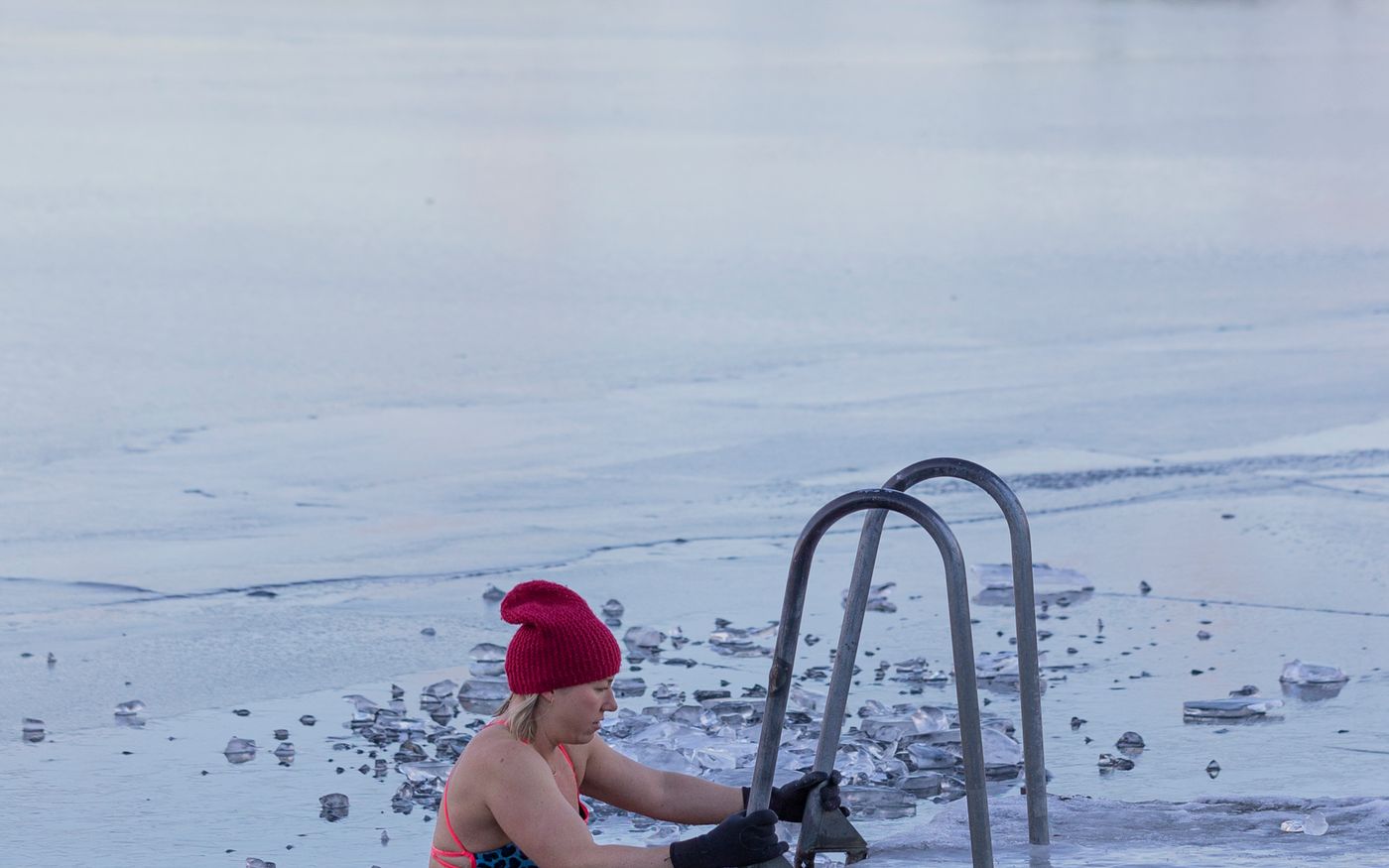 A woman entering a hole cut in a frozen lake by a ladder