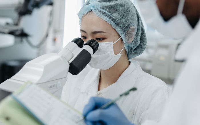 A researcher in a white coat looking through a microscope