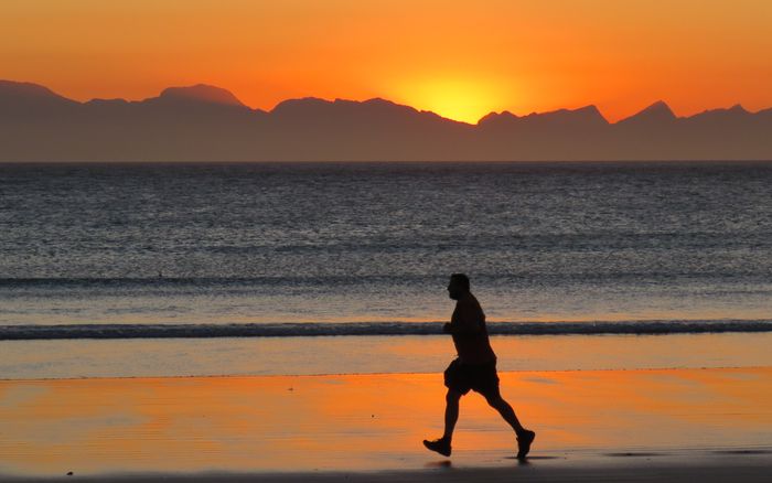 Silhouette of a person jogging along the shore at sunset