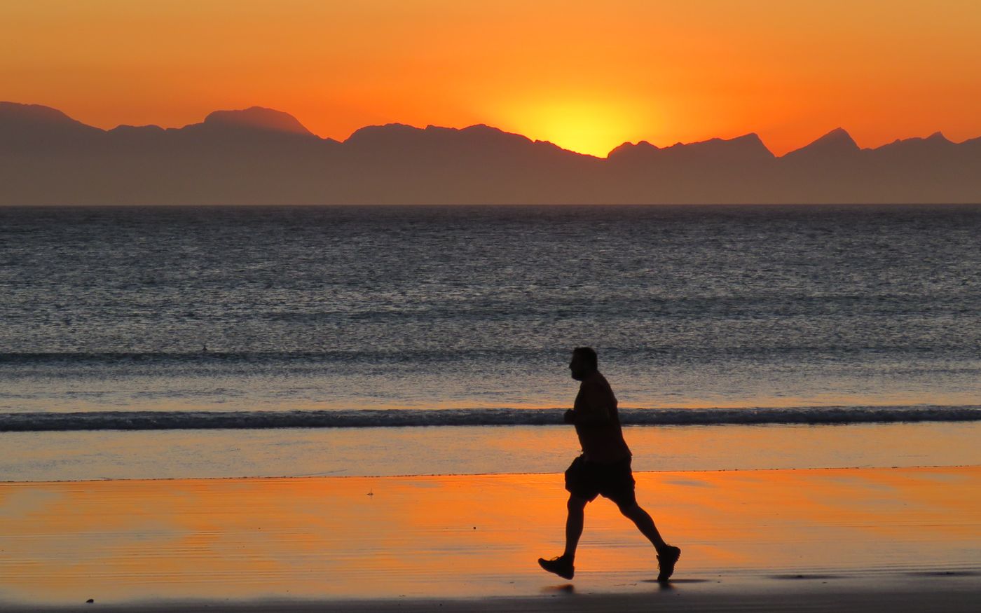 Silhouette of a person jogging along the shore at sunset