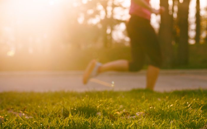 A woman jogging through a sunlit park at sunrise