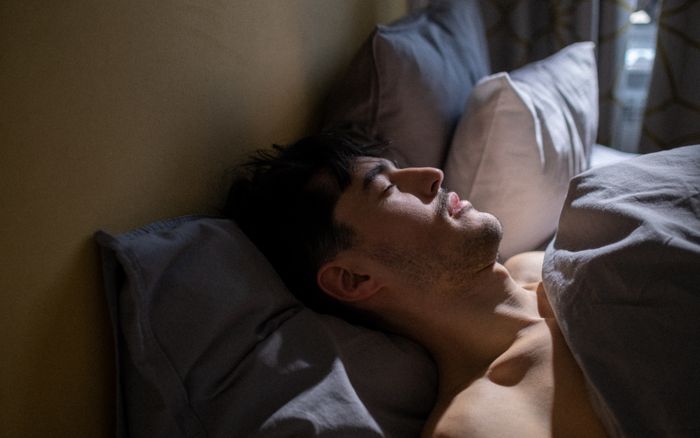A man asleep in a cool, dim bedroom with morning light