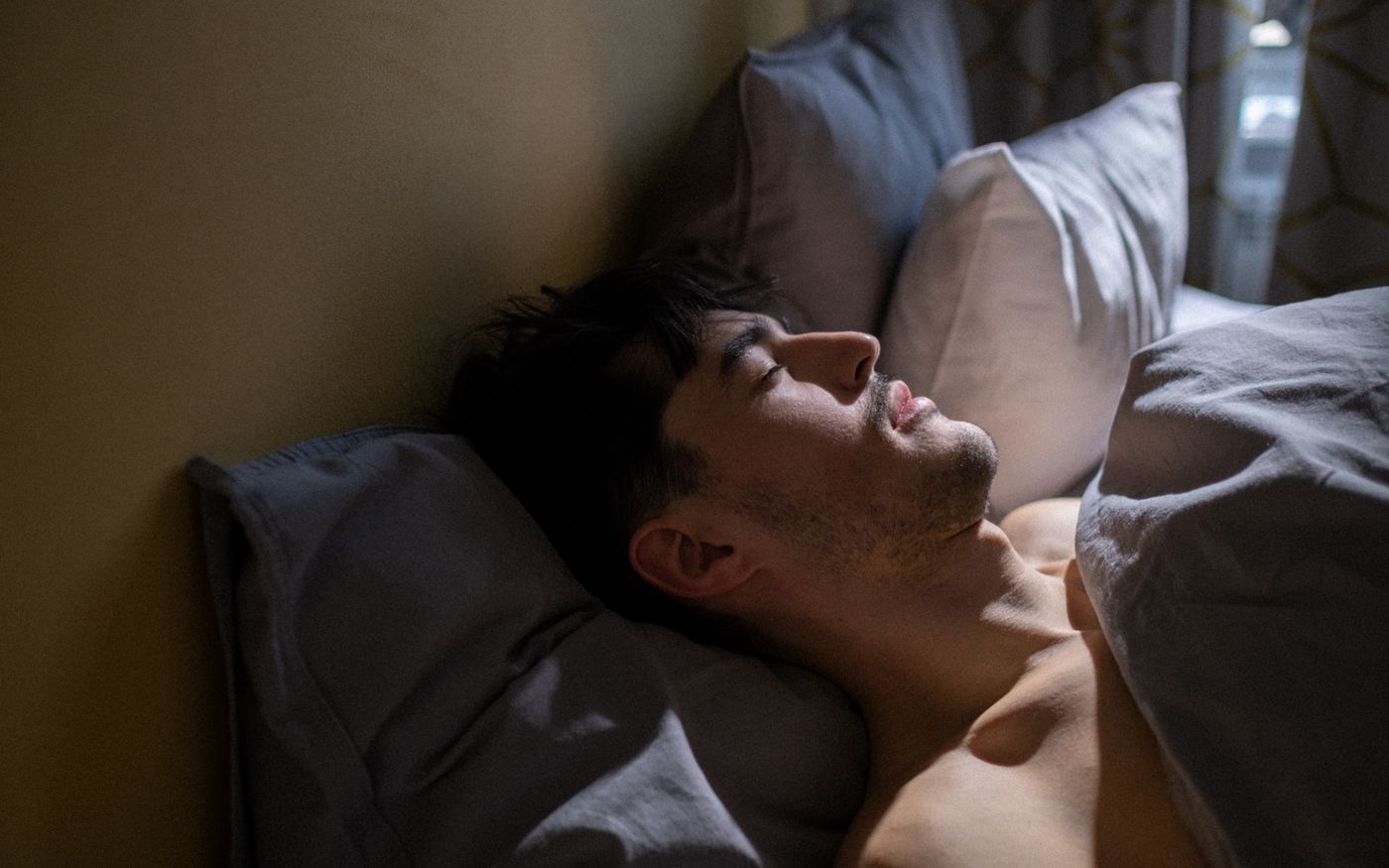 A man asleep in a cool, dim bedroom with morning light