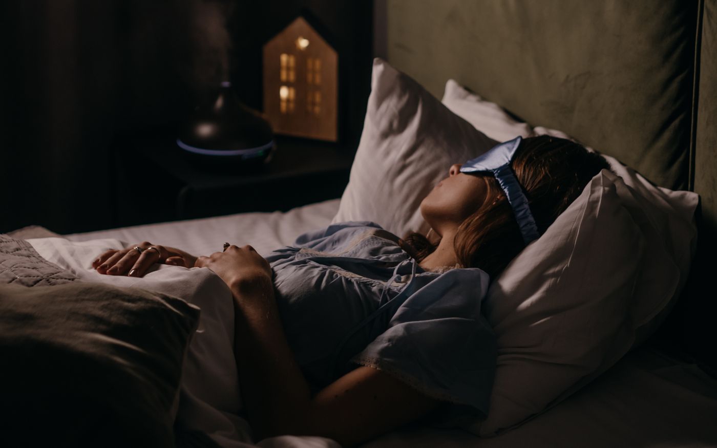 A woman asleep wearing an eye mask in a dim bedroom