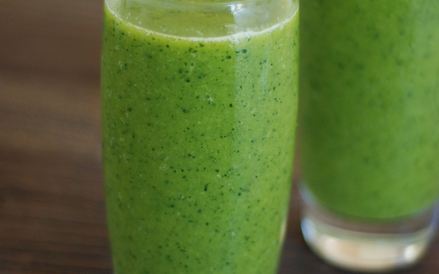 Two green smoothies in glasses on a rustic wooden table