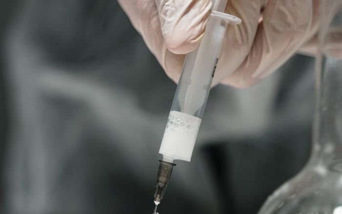 Gloved hands drawing liquid from a small vial with a syringe