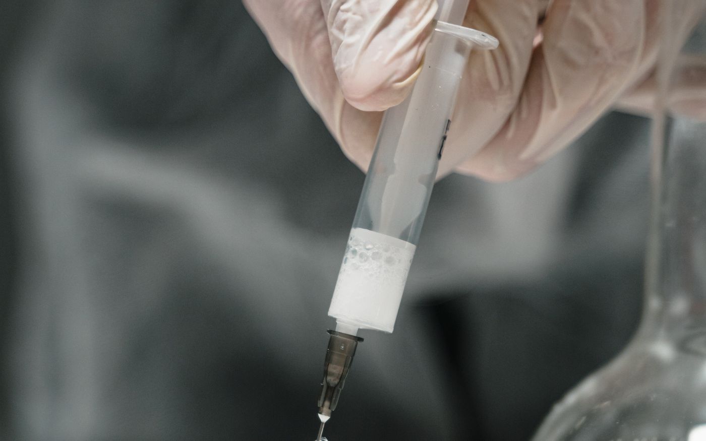 Gloved hands drawing liquid from a small vial with a syringe