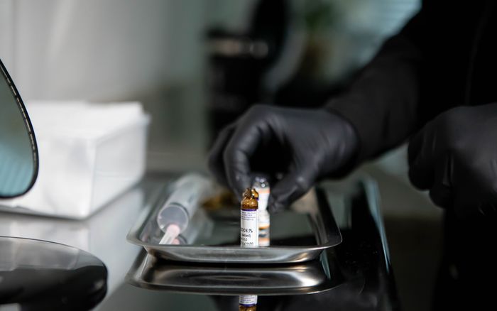 Gloved hands arranging small medicine vials and a syringe on a stainless tray