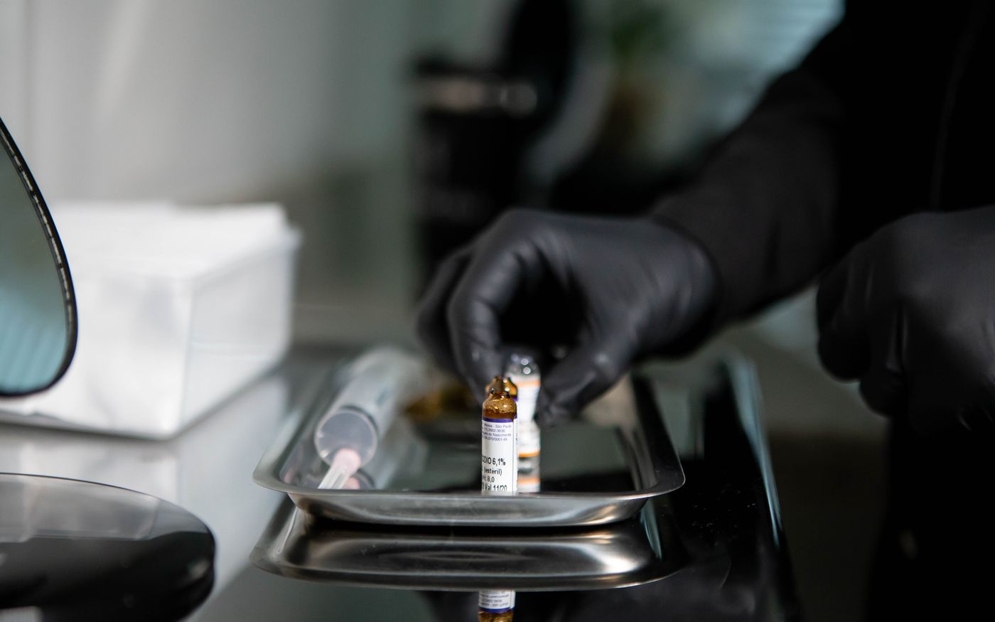 Gloved hands arranging small medicine vials and a syringe on a stainless tray